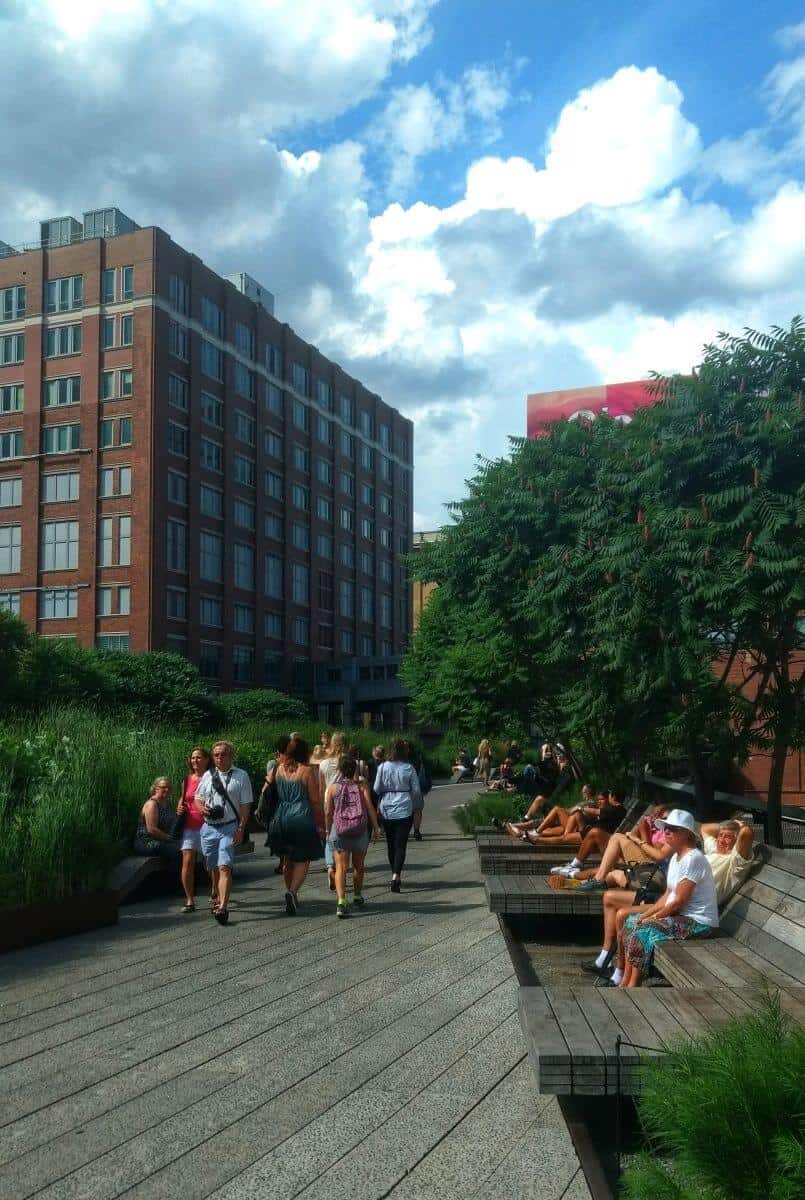 People walking on the New York City High Line with buildings and trees in the background.