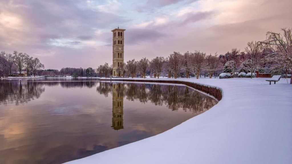 Bell tower next to a small lake with snow on the ground and a pink sky.