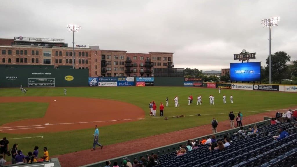 Baseball players warming up on a field with a green fence.