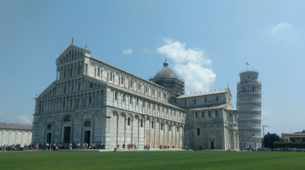 Large marble cathedral on a grassy field with the Leaning Tower of Pisa in the background.