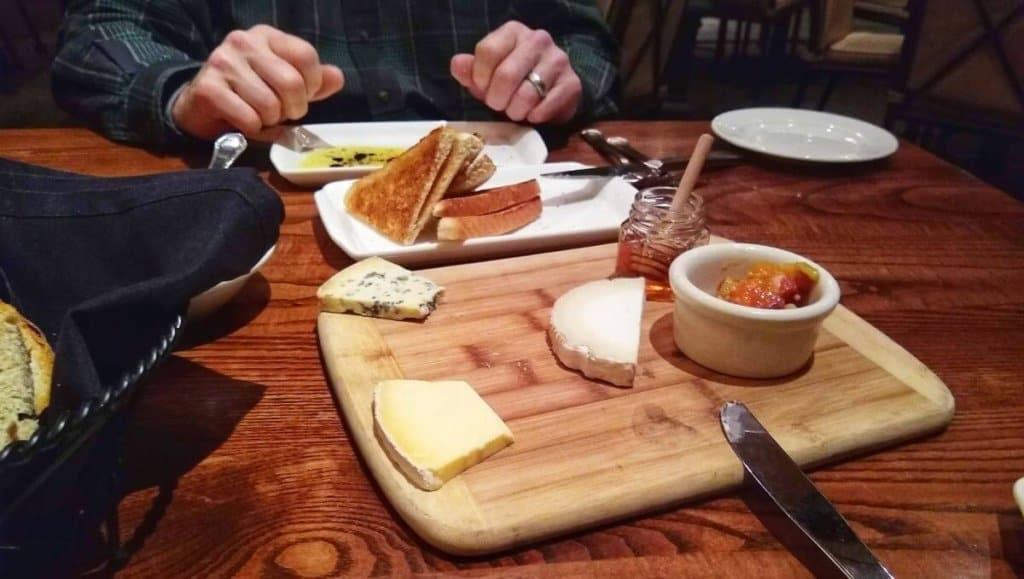 Wood board with several cheeses and honey.