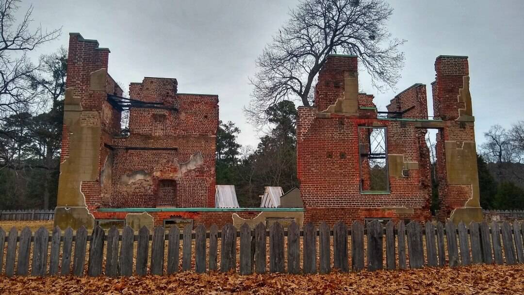 Ruins of a brick mansion with leaves on the ground and an old picket fence.