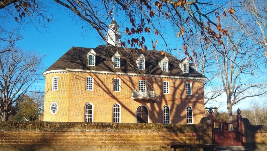 Tree casting shadows on the brick Colonial Williamsburg capitol building.