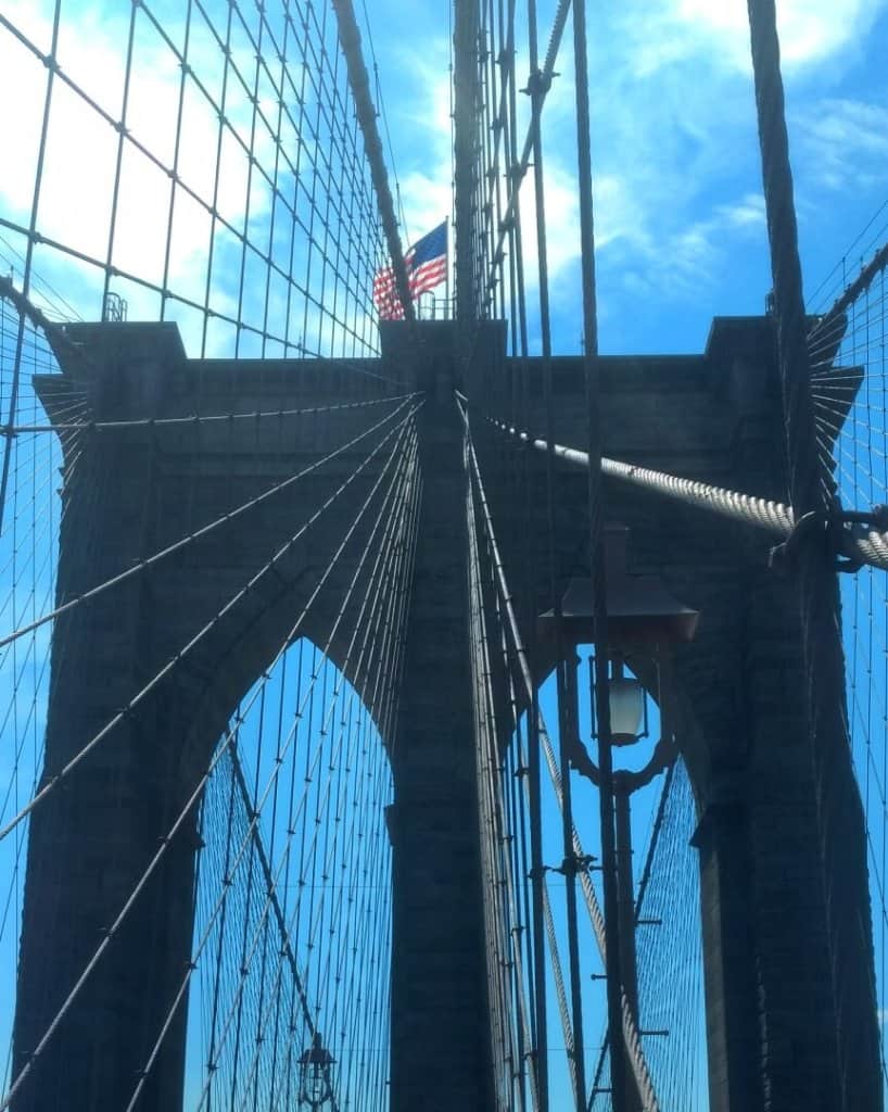 Brooklyn Bridge tower from below with blue sky and American flag.