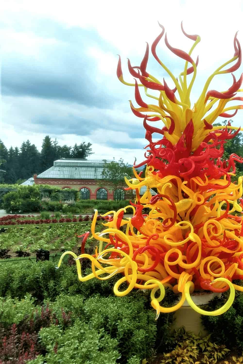 Colorful glass sculpture in a garden near a brick conservatory.