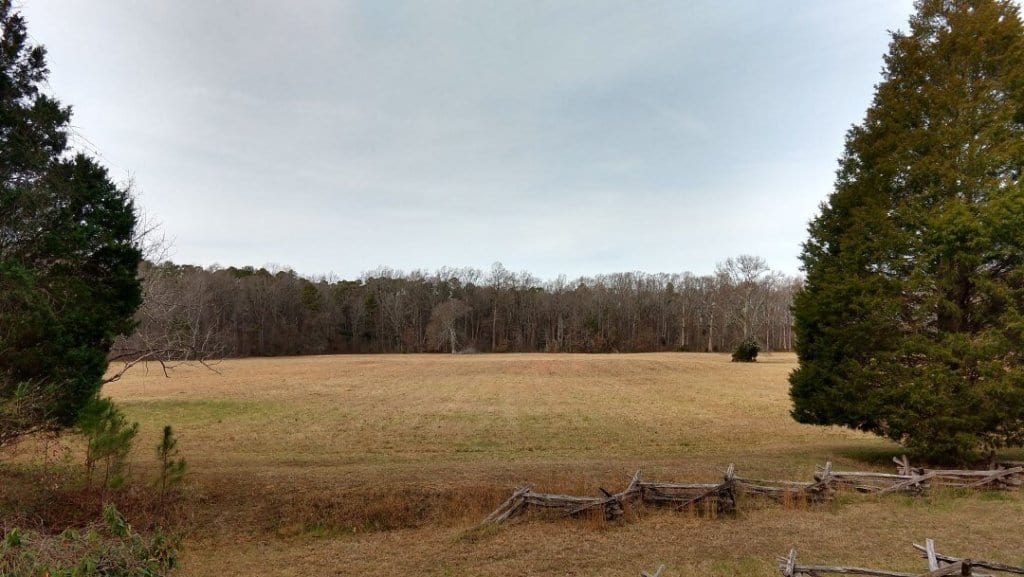 Open field surrounded by trees and old split-rail fences.