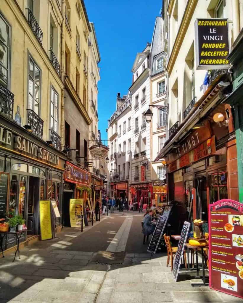Narrow street in the Paris Latin Quarter full of shops and cafes.