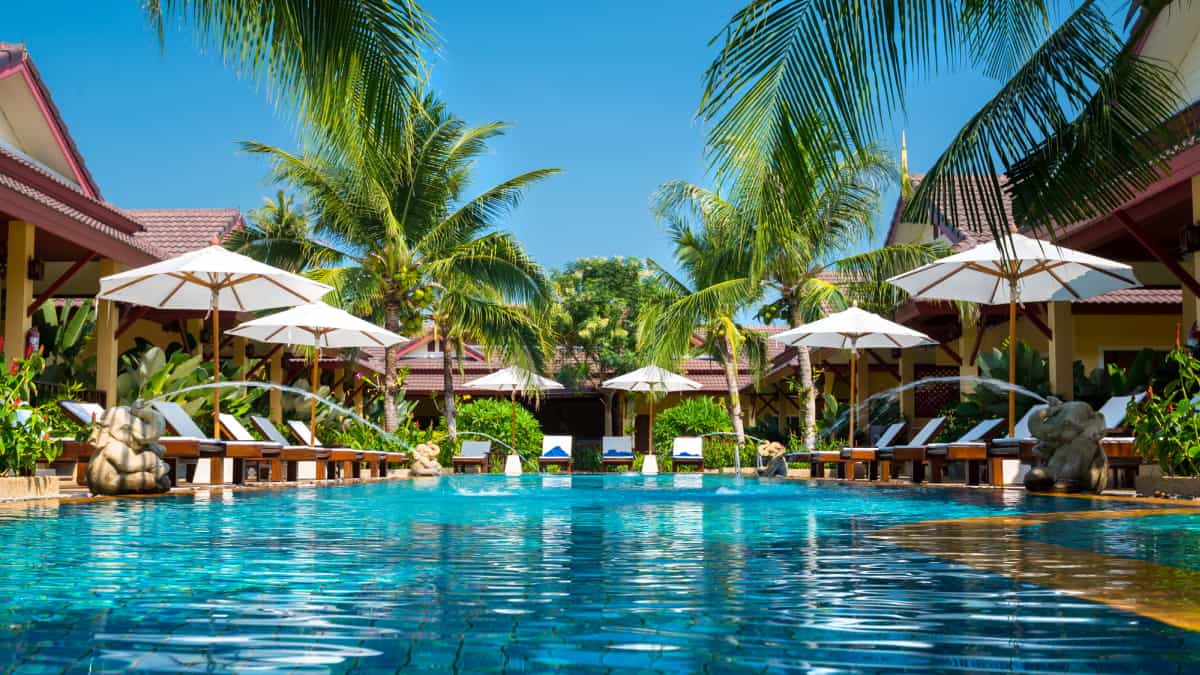 Beautiful hotel swimming pool with deck chairs, umbrellas and palm trees.
