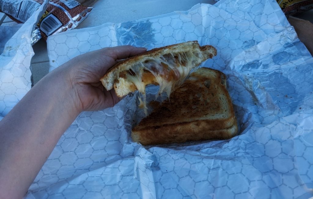Hand holding half of a grilled cheese sandwich with caramelized onions.