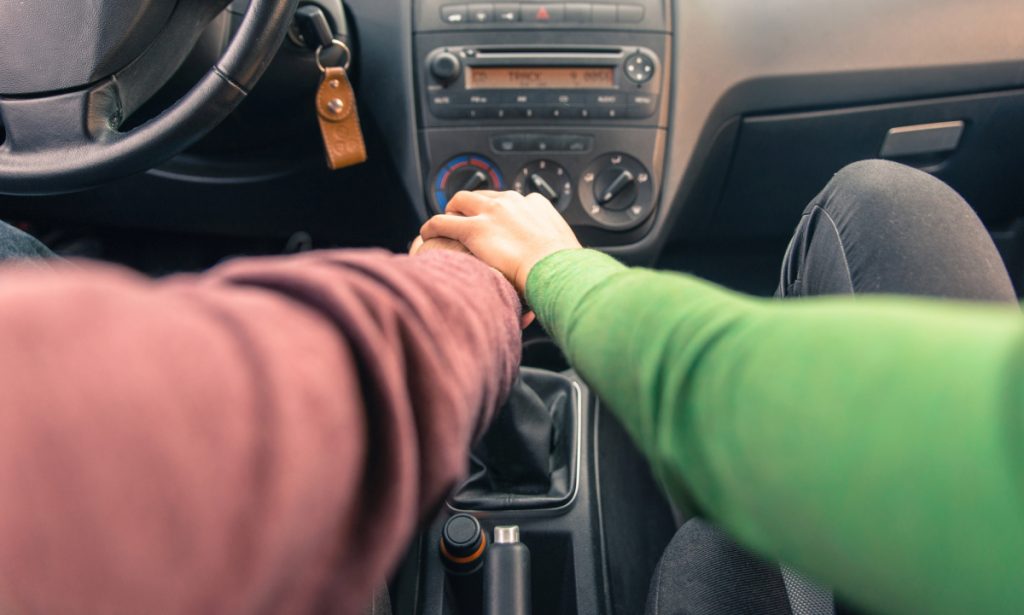 A man and a woman each have their hand on the gear shift of a car.