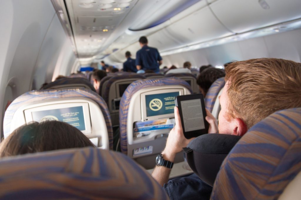 Rear view of airplane cabin with male passenger reading e-book on electronic reader during flight.