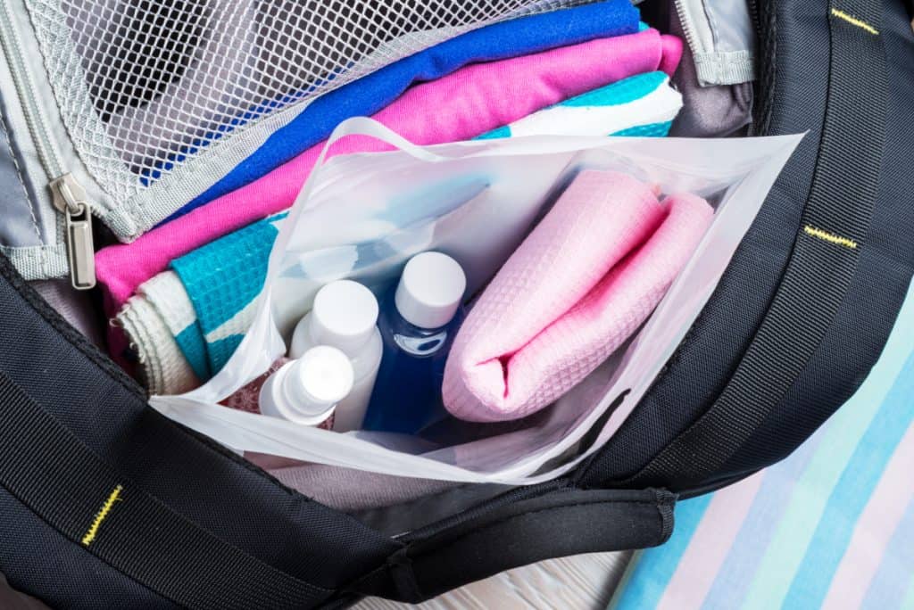 Set of travel bottles and towel in plastic bag inside a backpack