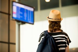 Young woman in straw hat with small backpack in airport terminal, looking at information board