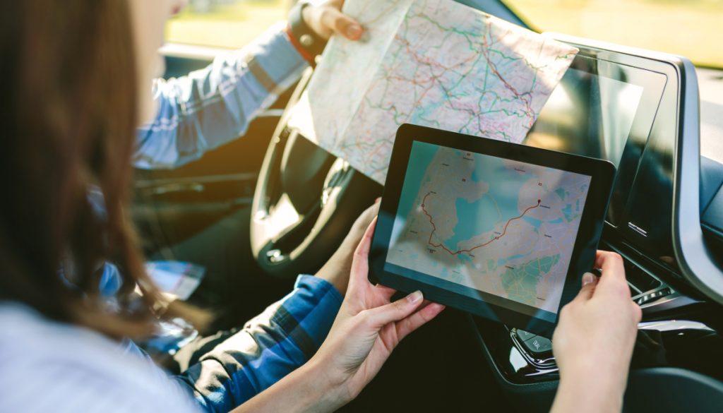 Young couple comparing a paper map and a gps navigator on the tablet sitting in the car