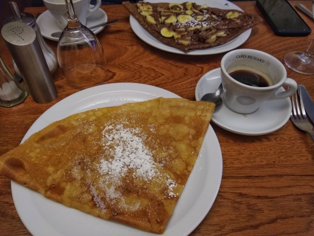 traditional butter a sugar crepe on a white plate next to a small cup of coffee