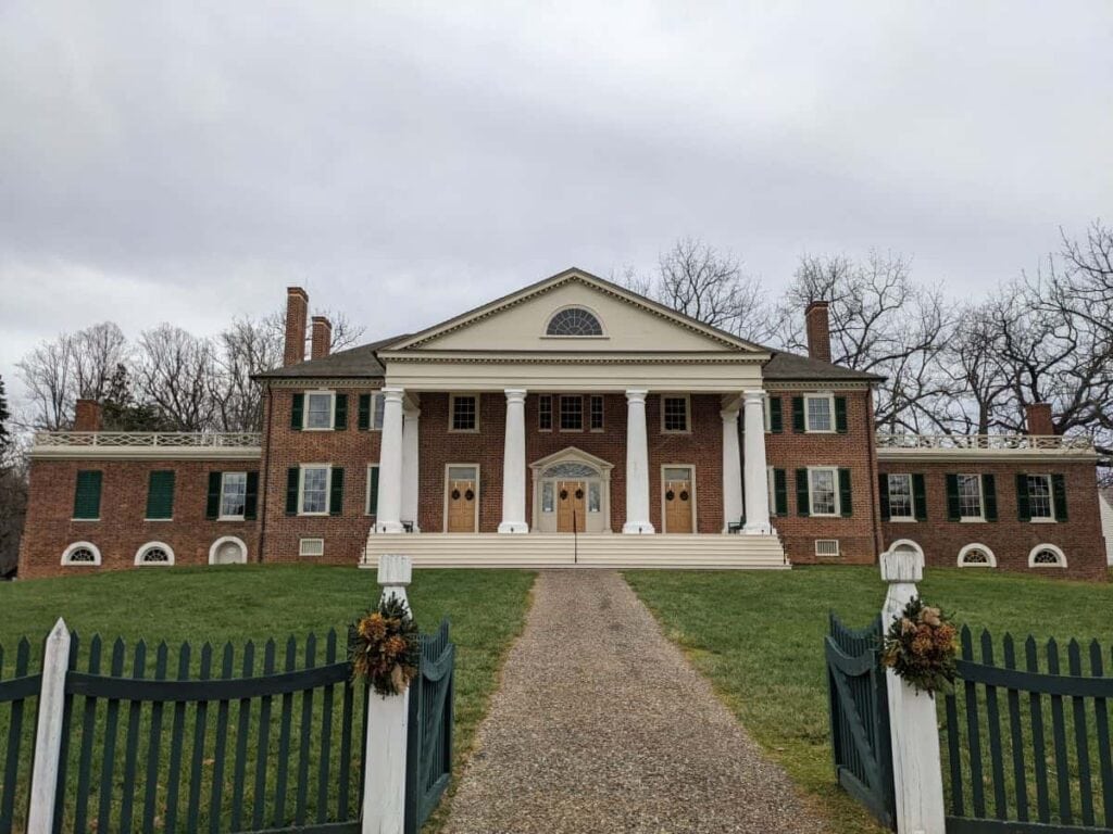 large brick house with columns in front and a green and white fence