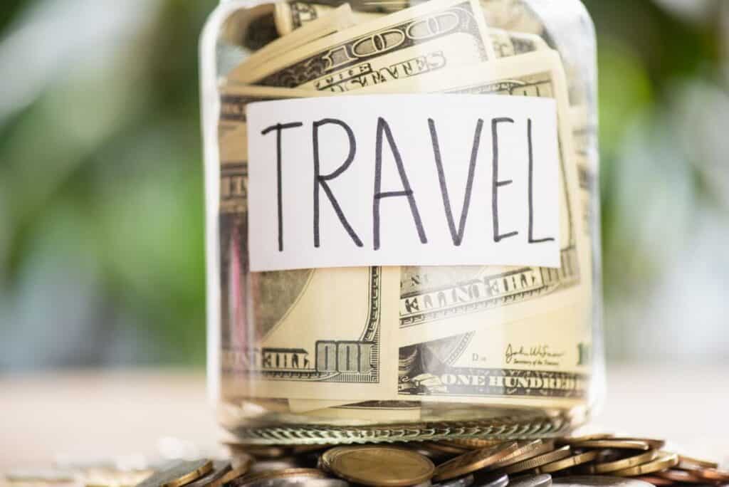 paper cash inside a clear glass jar labeled travel
