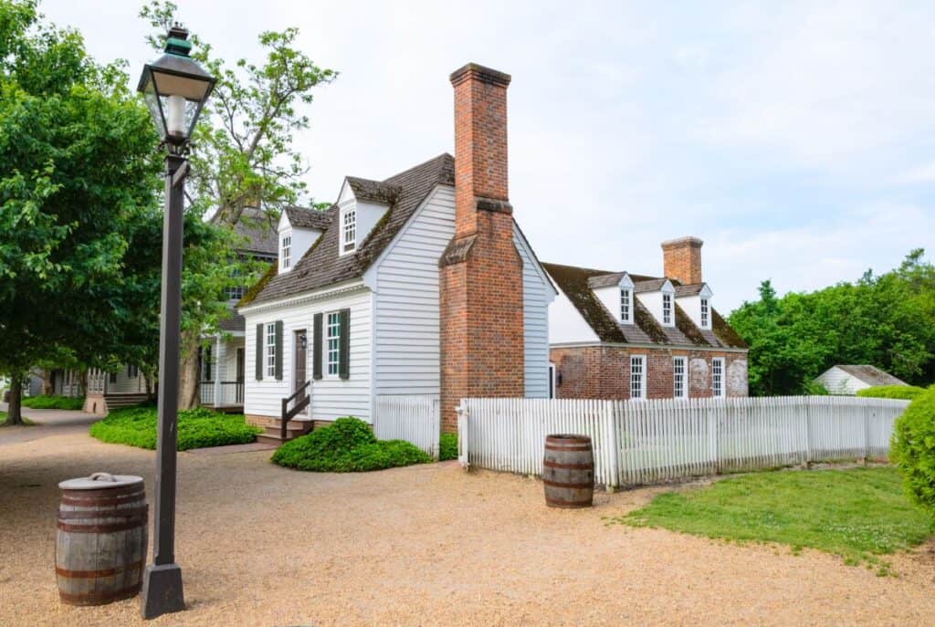 colonial style white cottage with a white picket fence and brick chimney