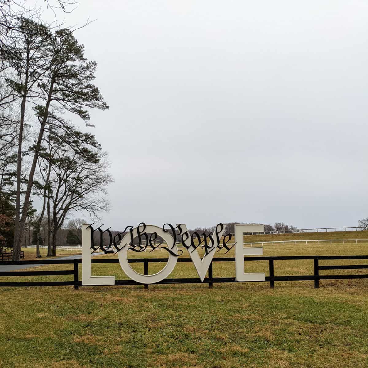 large sign mounted on a fence that reads we the people love