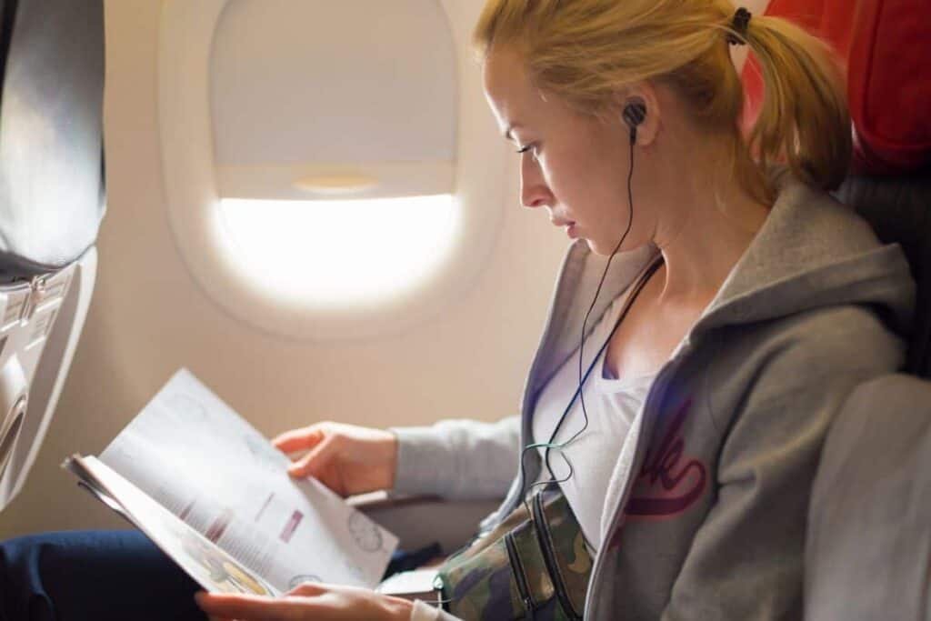 woman sitting on a plane wearing comfortable clothing and reading a magazine