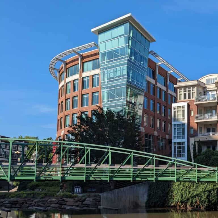 Large brick and glass building on the bank of the Reedy River in Greenville, South Carolina.