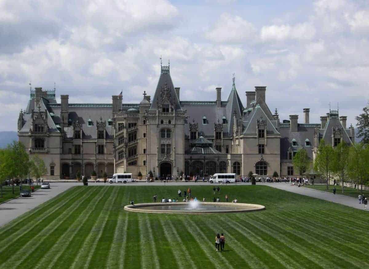 large stone house with a large green lawn and tourists roaming around