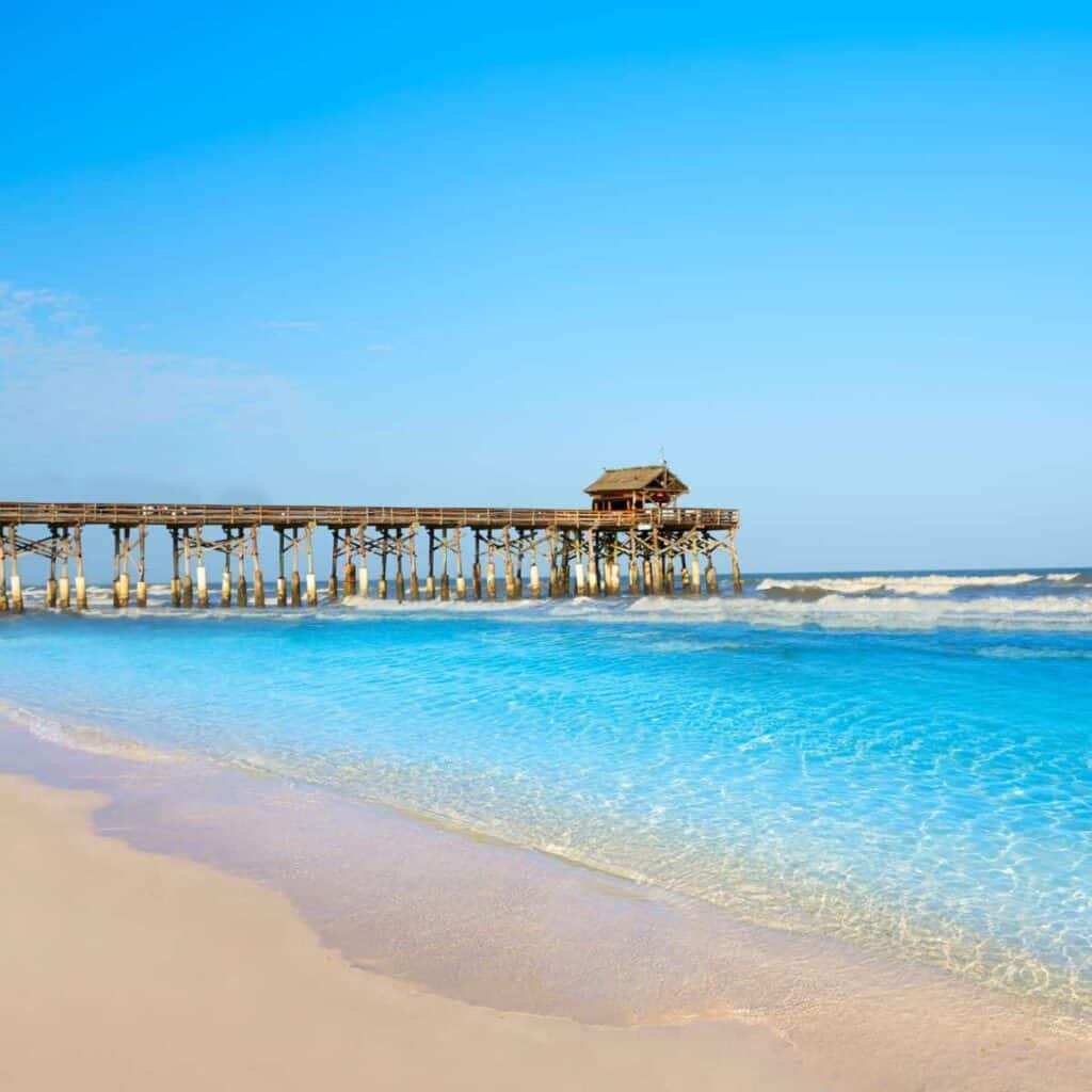 wooden pier out over clear blue water off a white sand beach in Florida