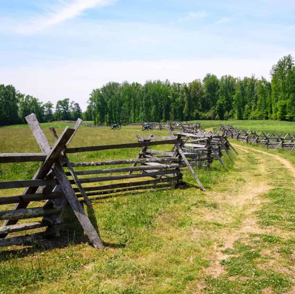 split rail fence with field guns in grassy field surrounded by trees