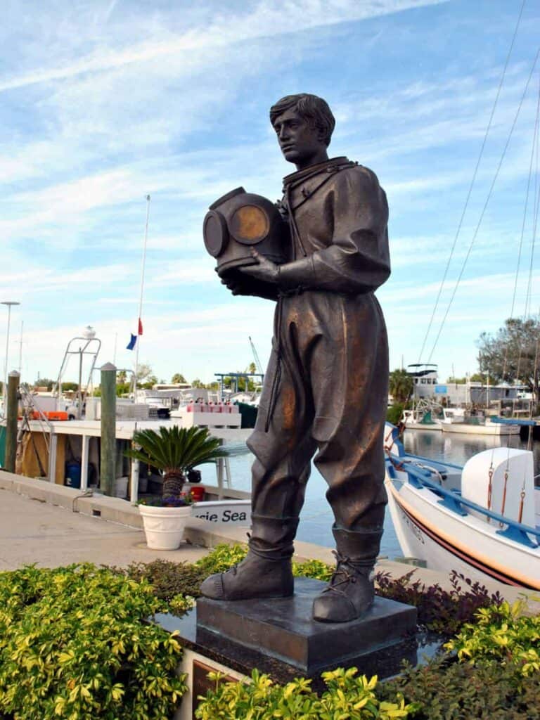 bronze statue of a man in a diving suit holding a helmet