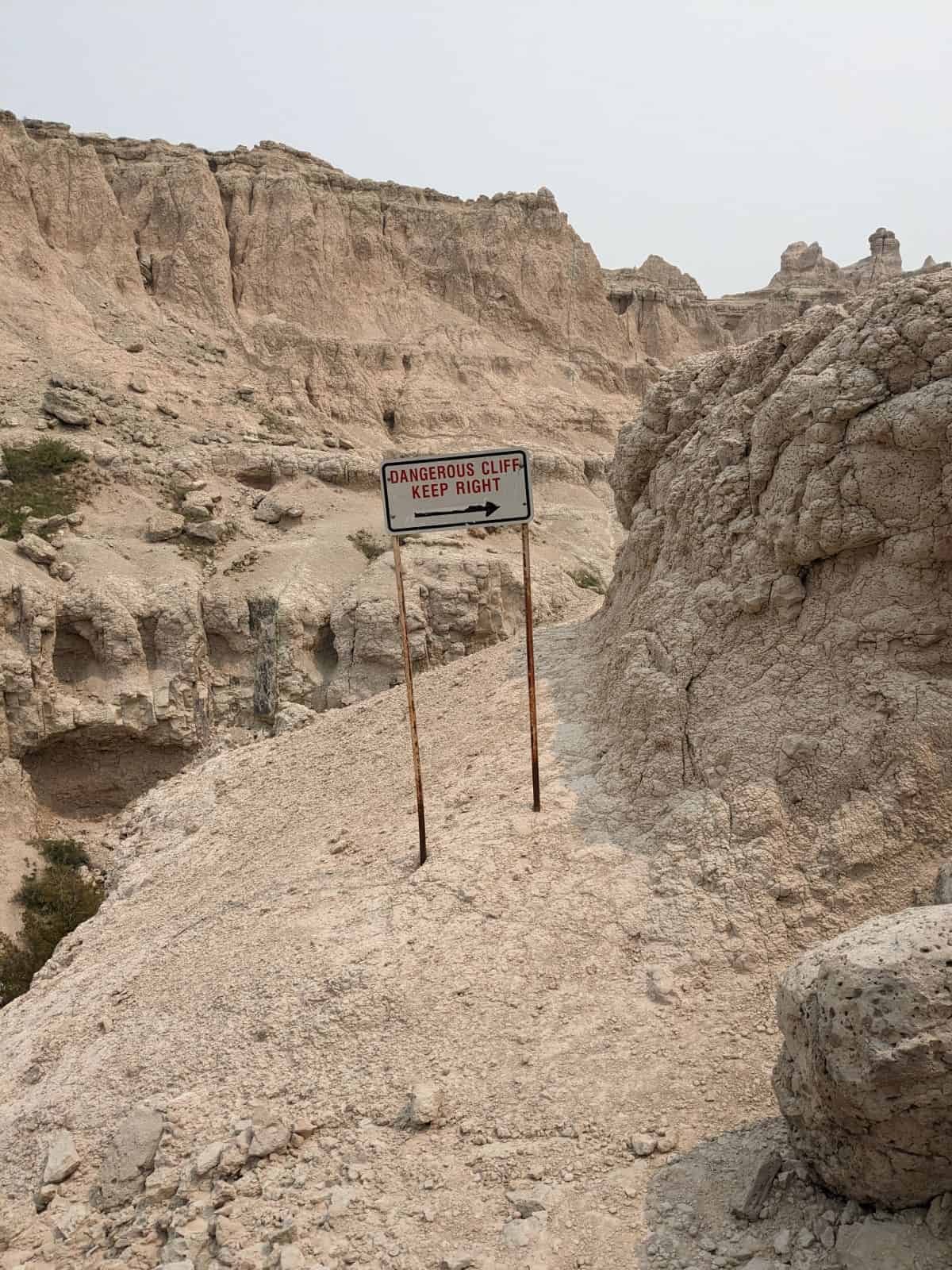 Metal sign on a rock cliff edge. Sign says dangerous cliff keep right.