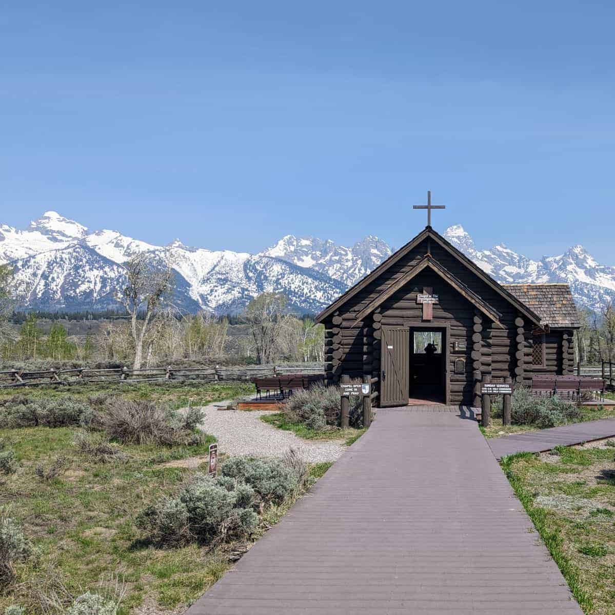 small log chapel with a wooden walkway up to the front door and the Teton Range in the background