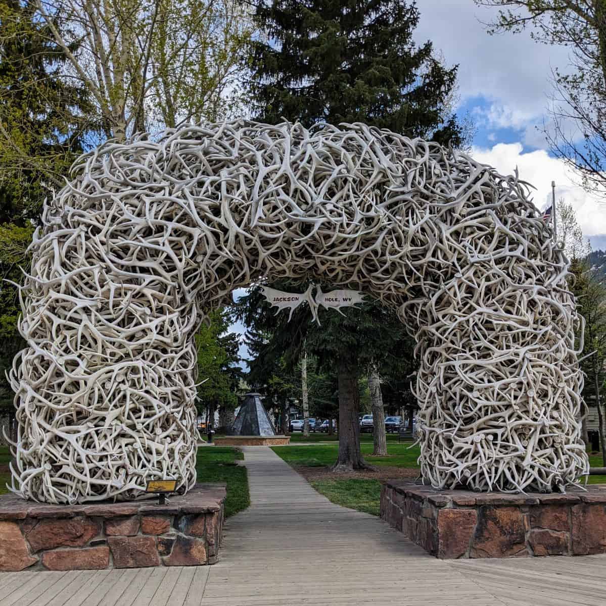 Large archway made of white elk antlers on a stone base over a wooden walkway at a town square.