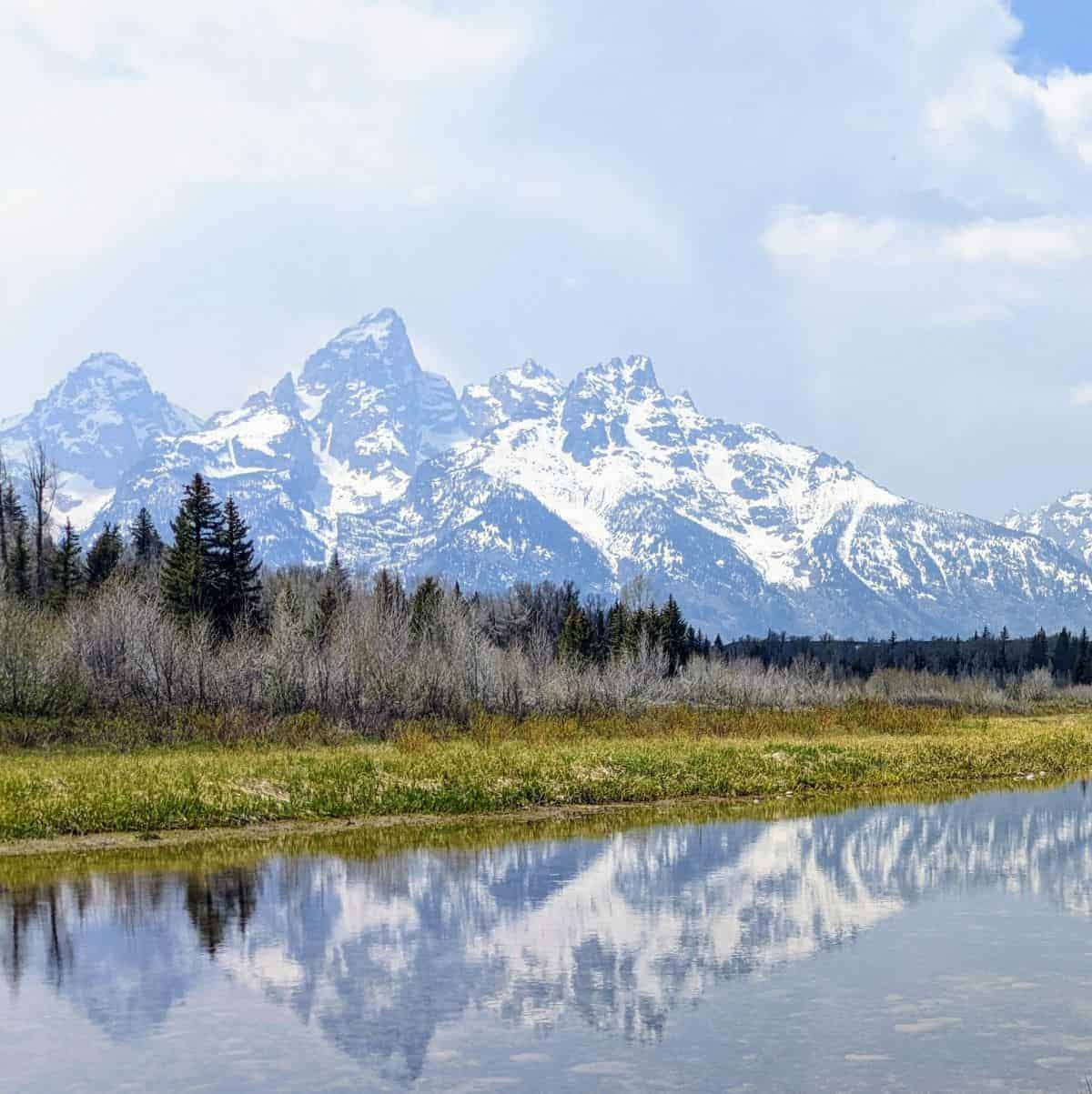 mountain range reflected in still river lined with grass and trees