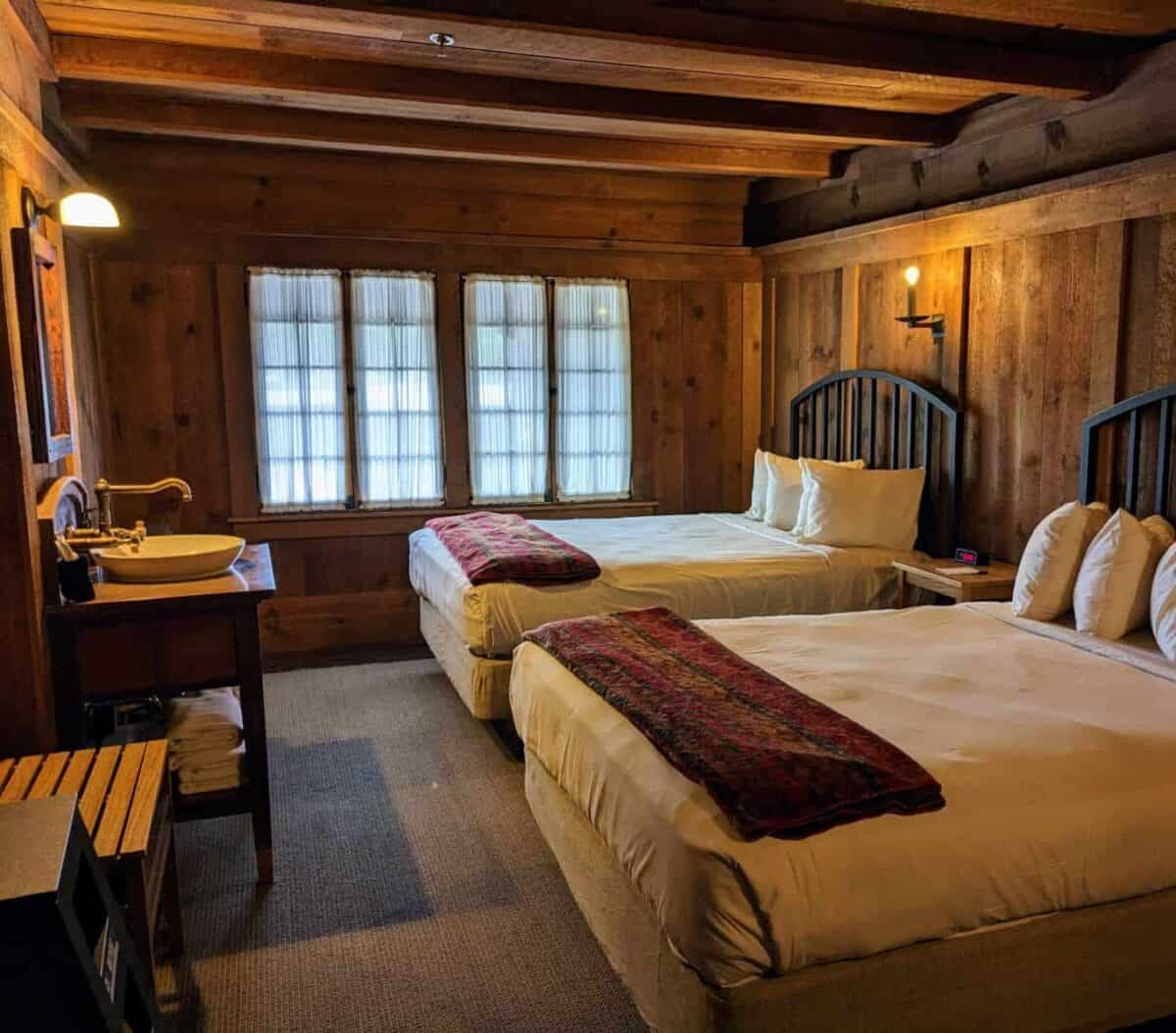 Two beds in an old-fashioned hotel room with wood-paneled walls and ceiling.