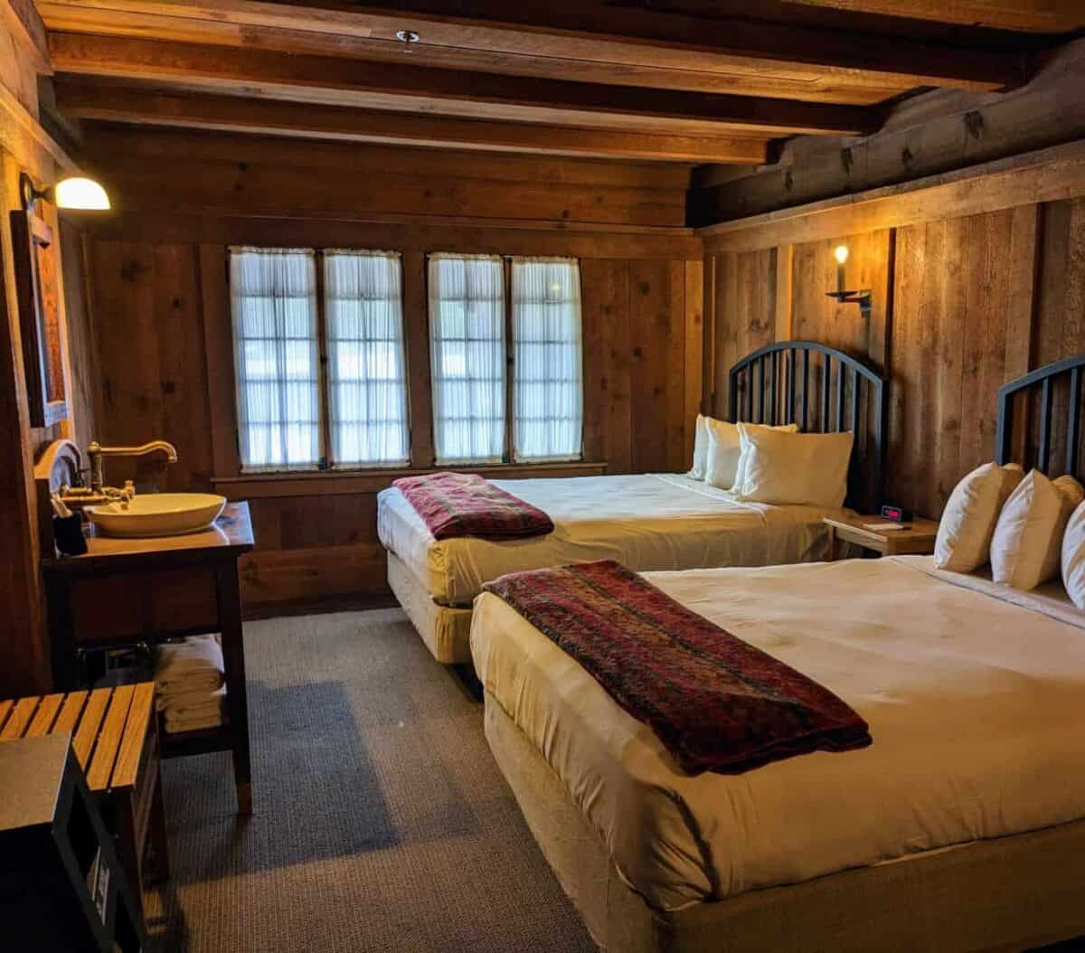 two beds and an old-fashioned looking washstand in a hotel room with wood walls