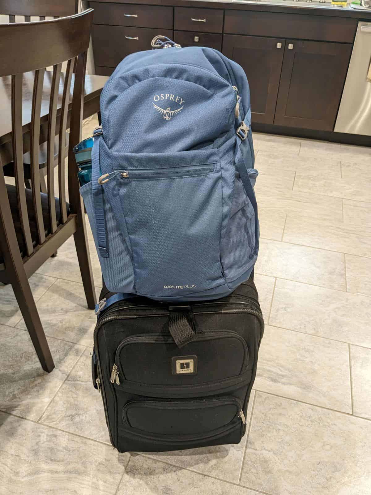 a blue Osprey backpack sitting on top of a small black roller bag