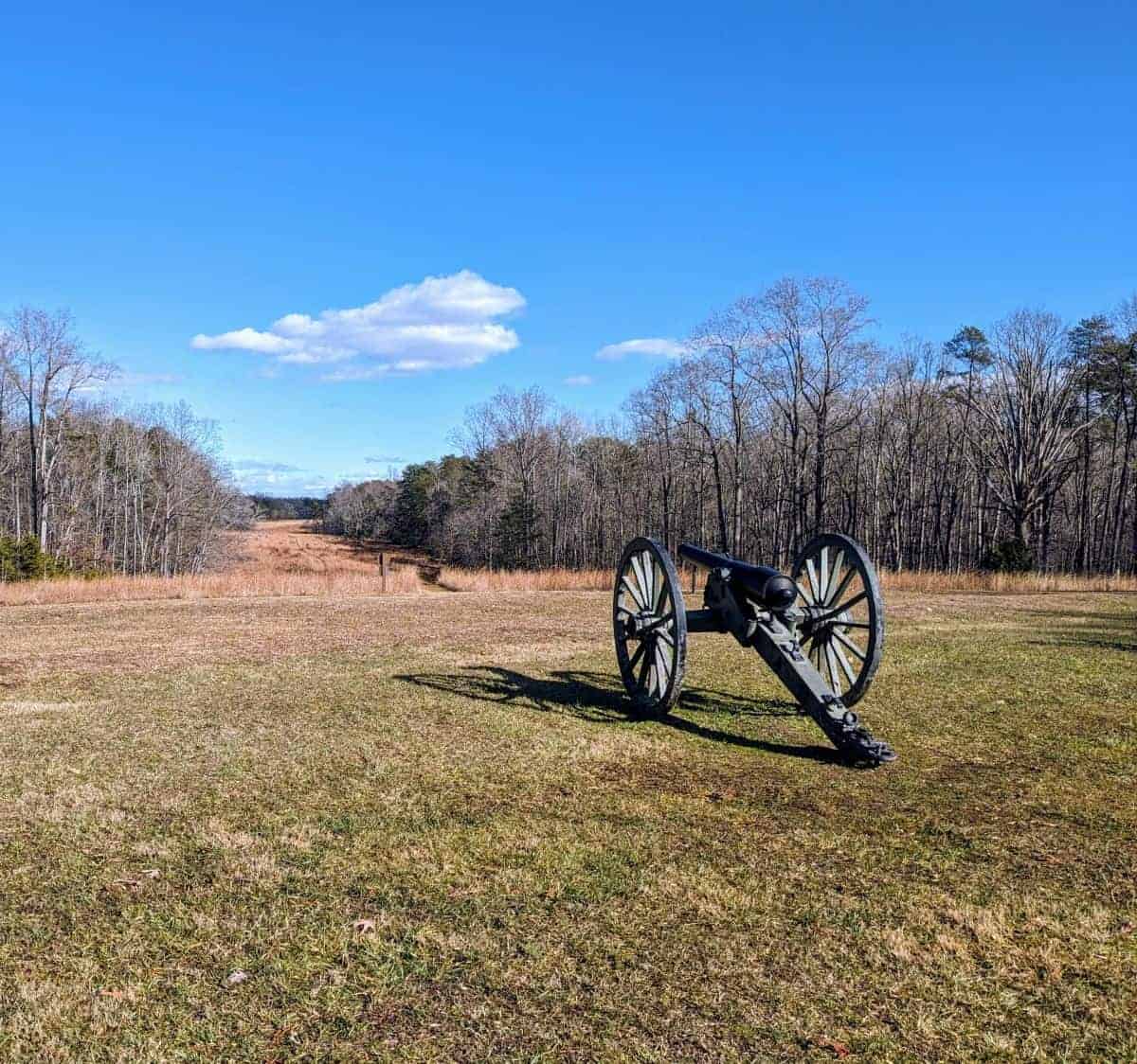 Old Civil War artillery piece sitting on a hill in a field. There is a blue sky. Many of the trees around are without leaves because it is a cold but sunny winter day.