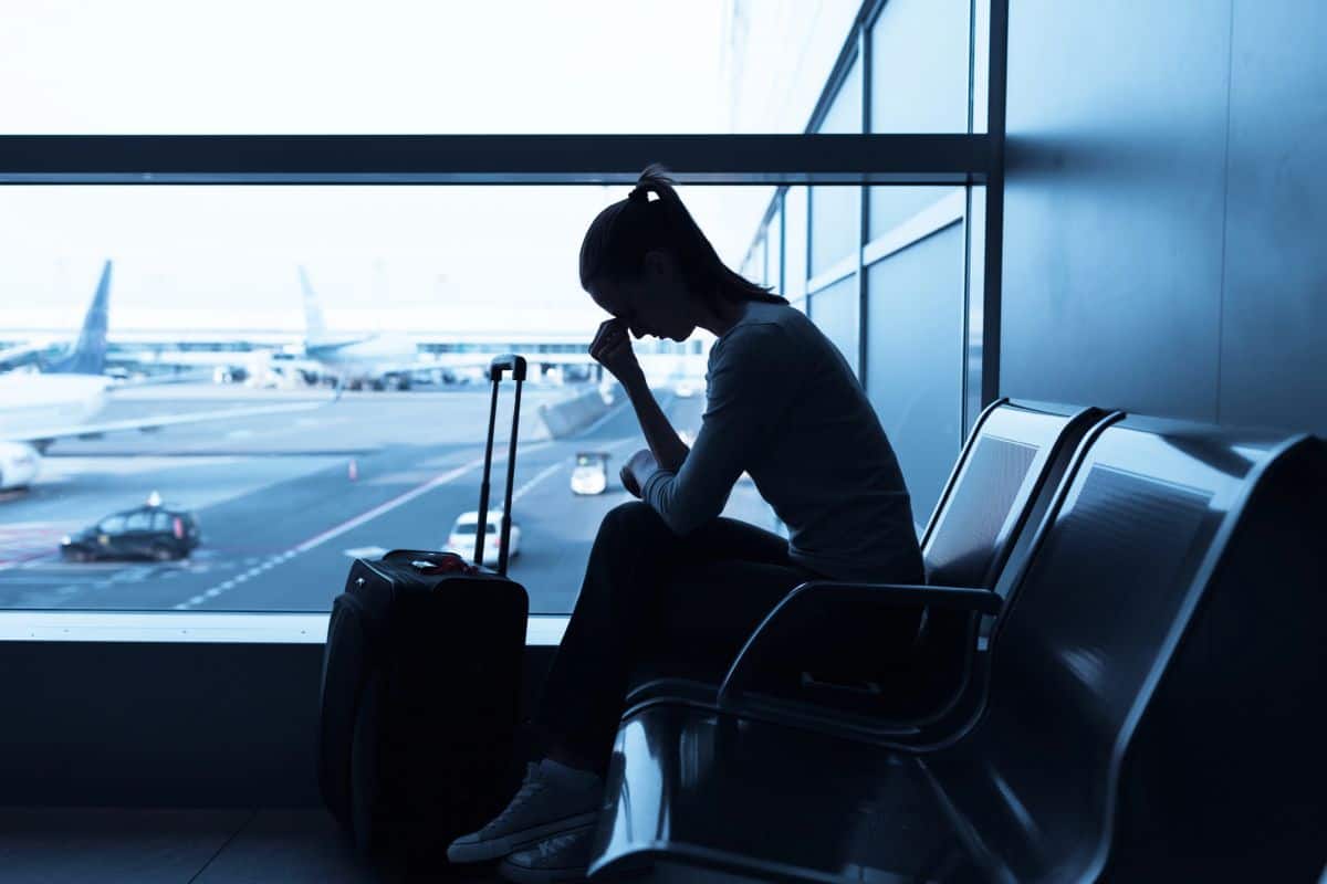 Frustrated woman waiting at airport with luggage.