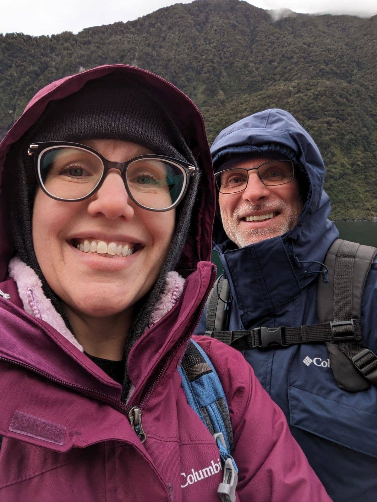 Hiking couple outdoors with mountains in background, dressed in waterproof gear for outdoor adventur.