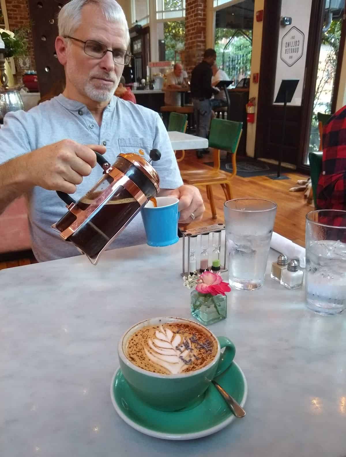 Man enjoying a coffee with food and drinks on the table.