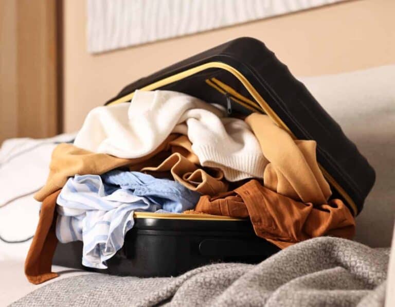 Travel packing essentials for a trip, with clothes spilling out of a black suitcase sitting on a sofa.