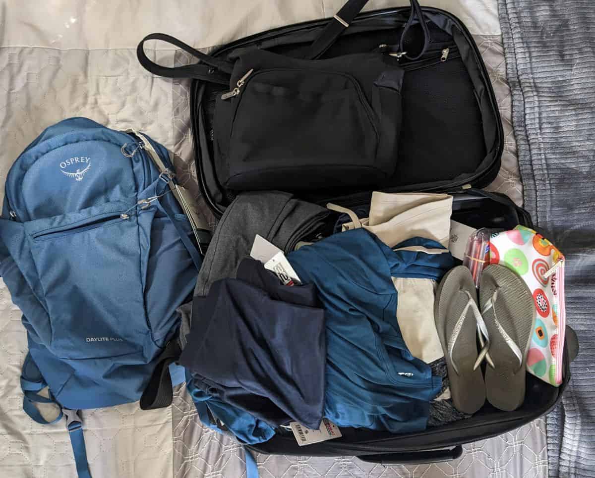 Open suitcase with backpack, clothing, and travel items ready for a two-week trip.
