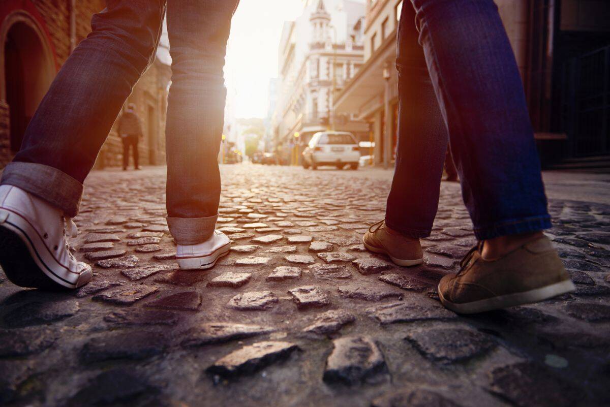 Urban street scene with pedestrians walking on cobblestone pavement at sunset.